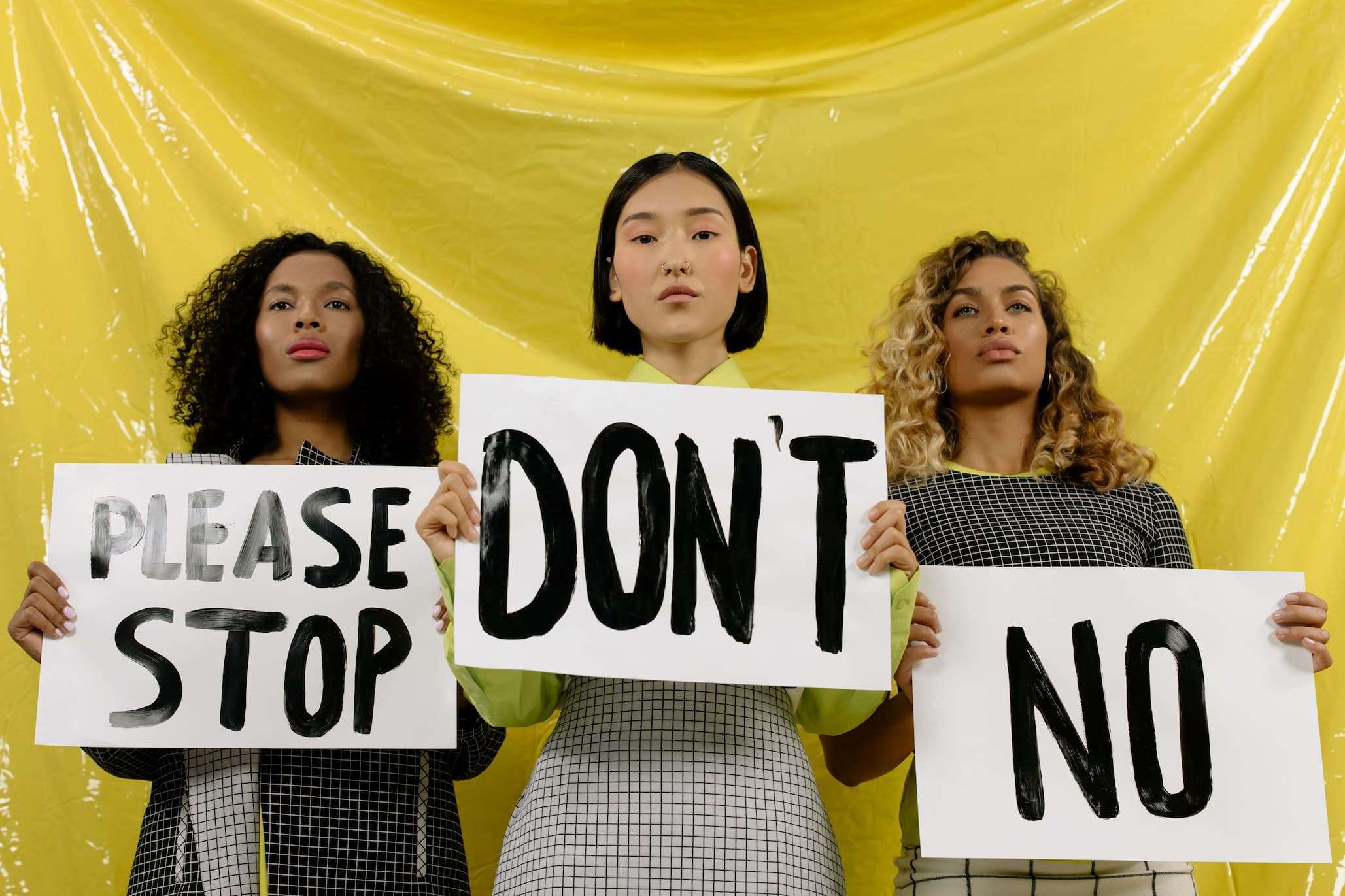 Women holding signs that say please stop, don't, and no.